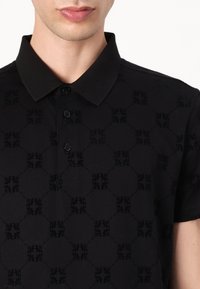 Svart polo skjorte med et teksturert mønster av sammenkoblede sirkler og blomsterformer, med krage og knappelukking.