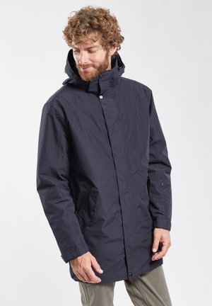 Veste imperméable marine avec un col montant et une capuche, dotée de poches latérales et d'une fermeture à pression à l'avant, fabriquée à partir d'un tissu lisse et durable.