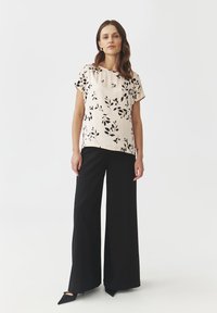 Cream short-sleeve blouse with a black leaf pattern, paired with black wide-leg trousers and pointed black shoes. Simple and modern design.