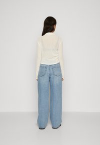 Top ușor, transparent, de culoare albă murdară, cu mâneci lungi, asortat cu blugi lejeri, cu talie înaltă, de culoare albastră deschisă, cu două buzunare pe spate.