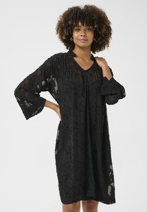 Black, knee-length dress made of sheer fabric with textured floral pattern, featuring a gathered neckline and loose, bell-shaped sleeves.