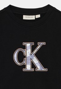 Sweat à capuche noir avec un grand logo « cK » en motif camouflage bleu-gris, bordé de orange clair, et avec un col côtelé.
