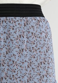 Jupe bleu clair avec une ceinture élastique noire, ornée d'un délicat motif floral en rose et marron. Tissu doux avec une texture fluide.