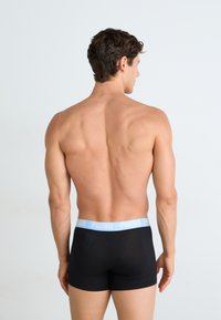 Boxerii negri cu un brâu de culoare albastru deschis pe care este inscripționat "PUMA". Modelul este văzut din spate, evidențiind un design neted și ajustat.