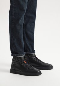 Czarne skórzane sneakersy typu high-top o teksturowanej powierzchni, z kolorowymi akcentami i sznurówkami, w parze z ciemnymi dżinsami.
