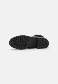 Semelle de botte noire avec un motif de crampons robuste, en matériau en caoutchouc durable, et une finition lisse avec une marque en relief.