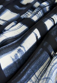 Tessuto bianco e nero con motivi astratti blu, caratterizzato da una superficie morbida e drappeggio fluido. Il design include forme geometriche di varia natura.