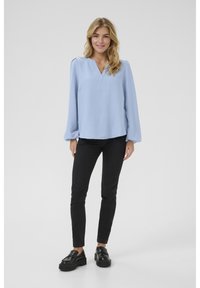 Blouse bleu clair à col en V et manches bouffantes, associée à un jean skinny noir et des mocassins à plateforme noirs. Texture du tissu lisse.
