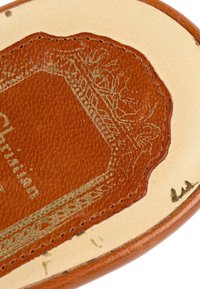 Gros plan sur la semelle intérieure en cuir beige et marron clair avec des coutures détaillées et une bordure décorative embossée, nom partiel de la marque visible.