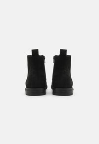 Bottines en daim noir avec un bout arrondi, une languette à l'arrière et des fermetures éclair latérales. Semelles en caoutchouc plates avec une finition texturée.