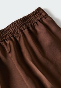 Bruine elastische taillebandbroek gemaakt van zachte stof met gegatherde stiksels rond de taille voor een comfortabele pasvorm.