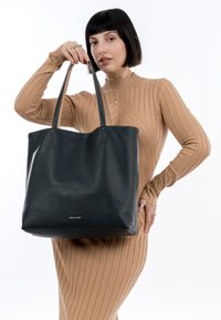 Sac fourre-tout en cuir noir avec une surface texturée, des poignées robustes et un design minimaliste. Présente un petit logo à l'avant.