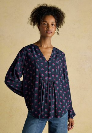 Marinebluse mit Blumenmustern, leichtem Stoff, V-Ausschnitt, Knopfdetails und langen Ärmeln, kombiniert mit blauen Jeans.