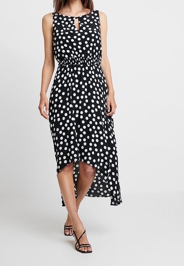 Robe noire à pois blancs avec un décolleté en trou de serrure, une taille élastique et un ourlet asymétrique. Fabriquée en tissu léger avec une texture lisse.