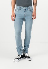 Lys blå denimjeans med slim fit, som har fem lommer, en standard midje og er brukt med svarte lave sneakers.