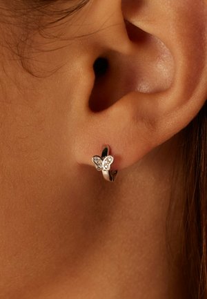 Zilveren, vlinder-vormige oorbel met ingewikkelde vleugeldetails en kleine edelstenen, ontworpen in een oorringstijl. Close-up van het oor.
