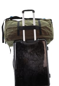 Green duffel bag with black straps sits atop a black hard-shell suitcase. The suitcase features a textured surface and a telescoping handle.