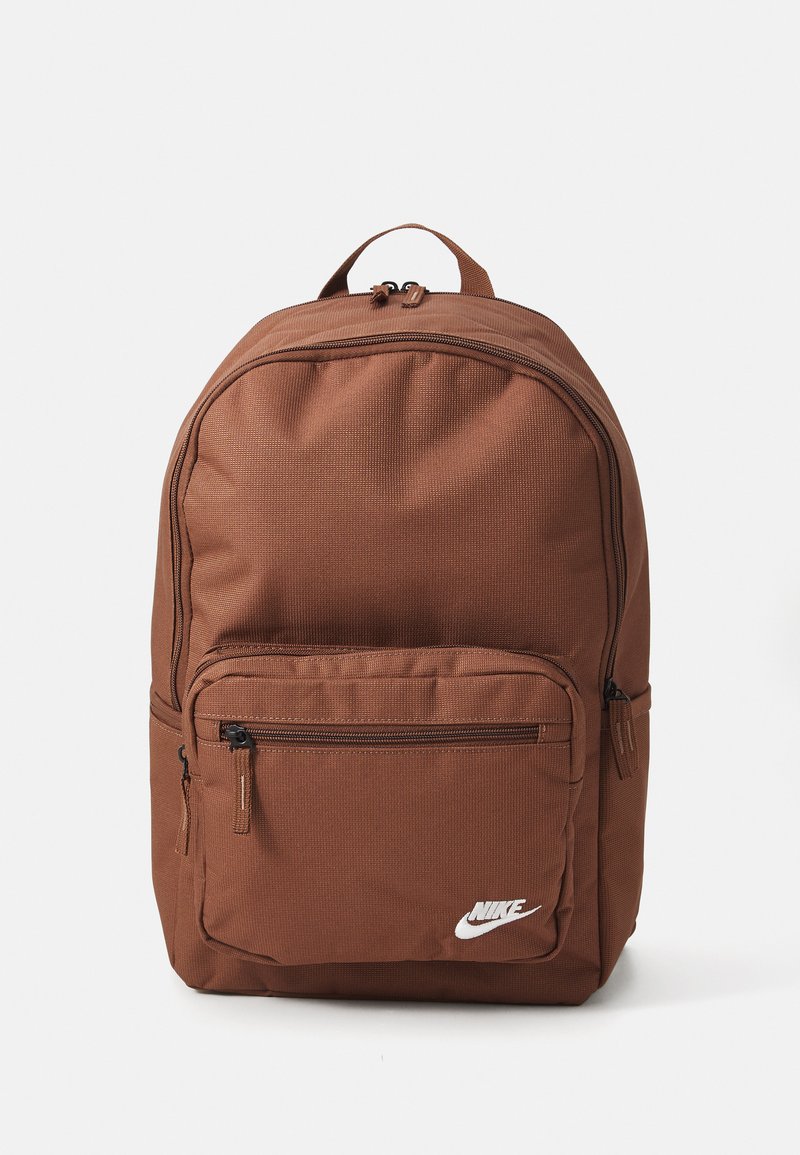 Pruunist kangast seljakott ümarate vormidega, eesmine lukuga tasku ja valge logo aktsent. Tekstuuriga materjal, kahekordsed tõmblukud peamise osakonna sulgemiseks.