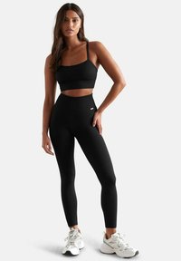 Completo di abbigliamento attivo nero a coste, composto da un top corto con spalline sottili e leggings a vita alta. Tessuto testurizzato con una vestibilità aderente.
