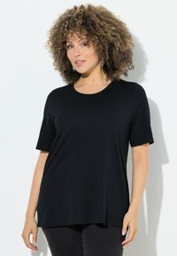 Camiseta negra de manga corta hecha de tela suave con cuello redondo, que presenta un corte relajado y dobladillo recto, combinada con pantalones oscuros.