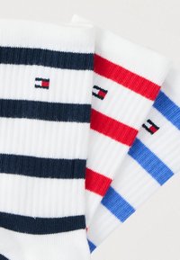 Τρία ζευγάρια λευκές ριγωτές κάλτσες με χοντρές οριζόντιες ρίγες σε ναυτικό μπλε, κόκκινο και γαλάζιο, κάθε μία με μικρό λογότυπο σημαίας.