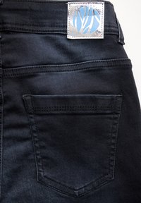 I jeans in denim neri presentano una singola tasca posteriore, un'etichetta del brand argentata con design blu, una texture liscia e cuciture pulite.