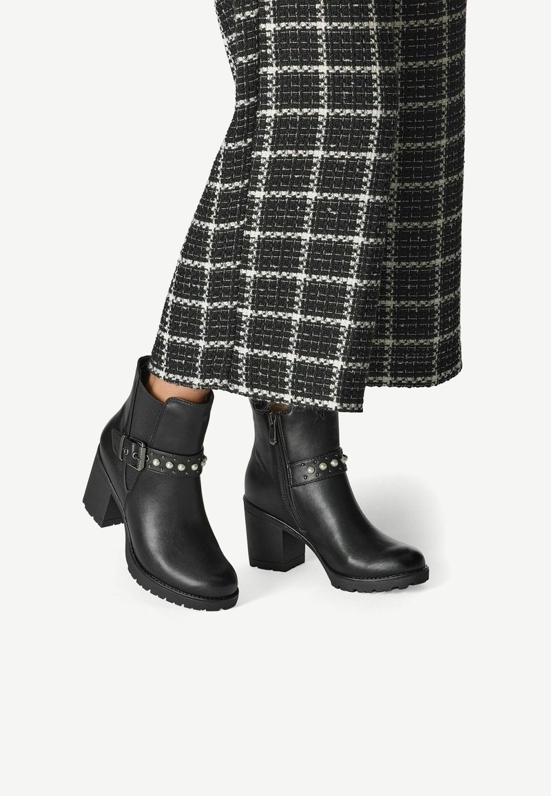 Black ankle boots made of smooth leather with a chunky heel, featuring a studded strap and side zipper for closure.