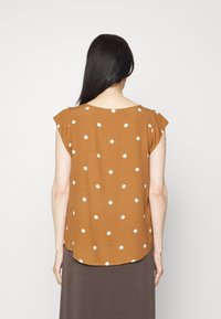 Blusa marrone a pois con maniche corte a sventola e scollatura tonda. I pois bianchi sono distribuiti uniformemente su tutto il tessuto.