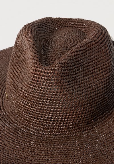 Chapeau fedora en paille tressée marron avec une calotte froissée et un large bord, présenté en gros plan sur un fond uni.