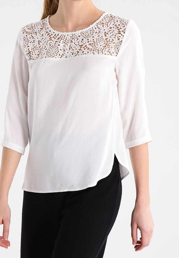 Vit blus med trekvartslånga ärmar, med en övre panel av spets och en slät nedre del, designad med en liten sidospringa.