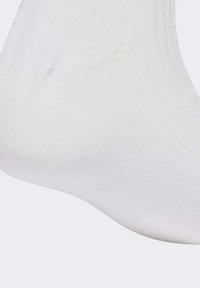 Bílá kotníková ponožka vyrobená z hladkého pleteného materiálu s žebrovaným designem na vršku. Oblast špičky je mírně zaoblená.