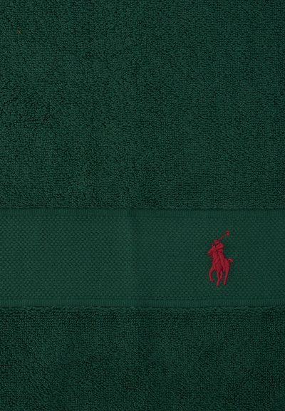 Σκούρα πράσινη πετσέτα με υφή οριζόντιας ταινίας και μικρό κόκκινο κεντημένο λογότυπο παίκτη πόλο πάνω σε άλογο στο κάτω δεξιό μέρος.
