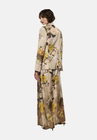 Blazer lungo beige con motivo floreale e gonna maxi coordinata. Tessuto setoso con fiori gialli e rosa, maniche lunghe e vestibilità rilassata.