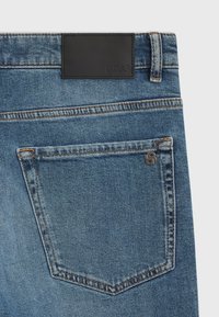 Vaqueros de mezclilla azul con un bolsillo trasero que presenta costuras naranjas y una etiqueta de cuero negro con la marca "BOSS" grabada en la cintura.