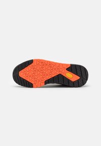 Suela de zapato con una suela de goma negra y naranja brillante que presenta patrones geométricos y un logo amarillo de Vibram cerca del arco.