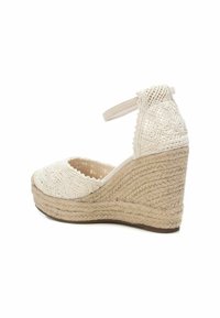 Zapato de cuña de esparto en beige, con parte superior de tejido texturizado con patrones intrincados, tira en el tobillo y tacón de yute trenzado.