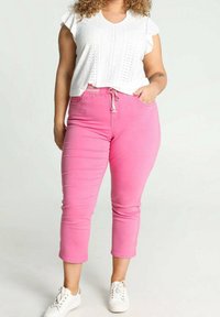 Světle růžové zkrácené džíny s tkaničkou, kombinované s bílým tričkem s krátkým rukávem, které má zdobení a vlnkované okraje.