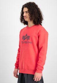 Felpa rossa in cotone con scollatura e polsini a costine. Presenta una stampa del logo nera al centro con tre strisce sopra di essa.