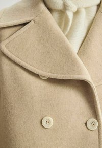 Manteau en laine beige mélangé avec un large col, design croisé et boutons crème. Présente une finition texturée et un tissu doux.