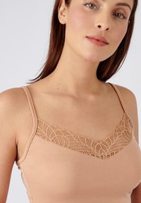 Canotta color carne con spalline sottili, decorata con pizzo sul scollo, realizzata in materiale morbido ed elasticizzato.