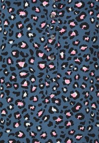 Camisa de estampado de leopardo en tela azul con manchas negras, rosas y blancas. Presenta un cierre de botones con una textura suave y un diseño casual.