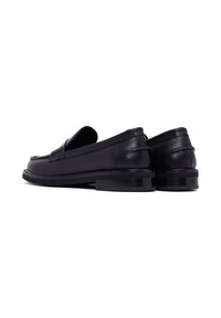 Mocasines de cuero negro con un acabado suave, punta redondeada y tacón bajo apilado. Presentan un acento texturizado en el empeine y detalles de costura mínimos.