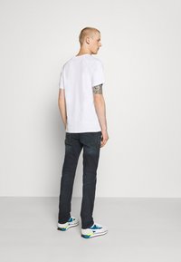 T-shirt branca de mangas curtas, jeans de ganga e ténis de desporto. Inclui um braço tatuado e vista traseira. Design simples e casual.