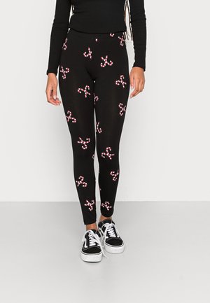 Leggings noirs avec un motif de cannes en sucre répété en rouge et blanc. Fabriqués en matériau extensible, conçus pour le confort et la flexibilité.