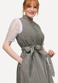 Abito grigio a fantasia con collo alto, maniche a sbuffo in pizzo e una cintura legata in vita con accenti a righe e disegni floreali.