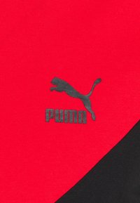 Červená látka má černé logo Puma s designem skákajícího tygra. Materiál je hladký na dotek a má čistý, sportovní vzhled.