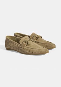 Beige perforierte Wildleder-Loafer mit runder Spitze und dekorativer Hardware in Goldton. Flache Gummisohle für einfachen Tragekomfort.