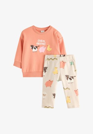 Pfirsichfarbener Pullover mit "Farm Friends"-Grafik und cremefarbene Hose mit Tiermustern in Rosa-, Braun- und Gelbtönen.