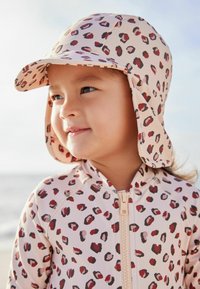 Cuffia da nuoto e rash guard con stampa leopardata in tonalità di rosa e rosso, caratterizzati da una cerniera frontale e una protezione sul cappuccio.