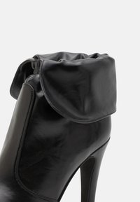 Μαύρο δερμάτινο ankle boot με ψηλό τακούνι που διαθέτει χαλαρή κορυφή, λεία υφή και στρογγυλή κολάρα. Ο σχεδιασμός περιλαμβάνει εφαρμοστή σιλουέτα.